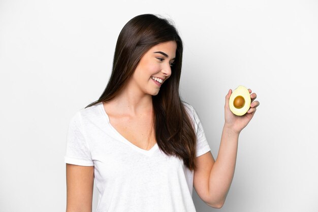 Giovane donna brasiliana in possesso di un avocado isolato su sfondo bianco con felice espressione