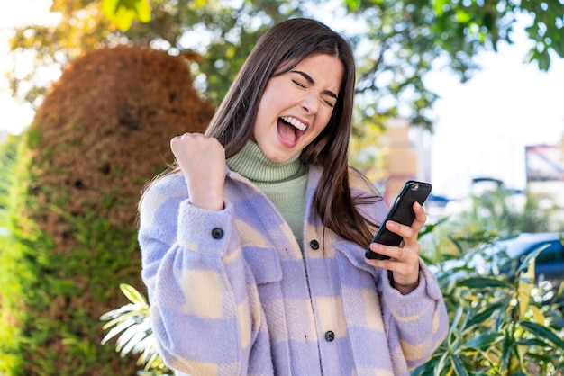 Giovane donna brasiliana in un parco con il telefono in posizione di vittoria