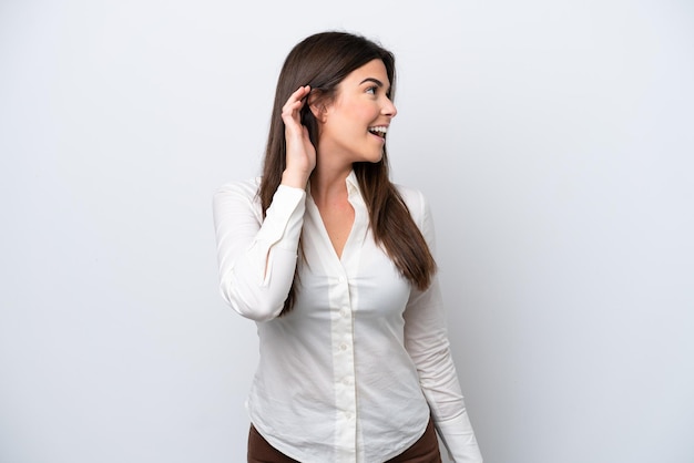 Giovane donna brasiliana isolata su sfondo bianco che ascolta qualcosa mettendo la mano sull'orecchio