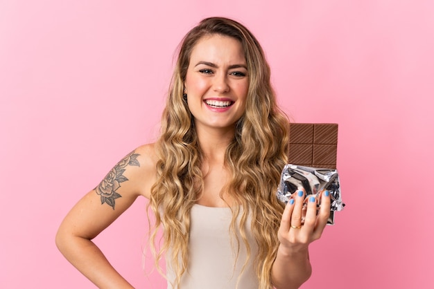 Giovane donna brasiliana isolata sulla parete rosa che prende una compressa di cioccolato e felice