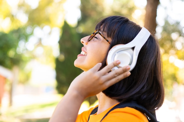 Giovane donna bruna all'aperto ascoltando musica e cantando