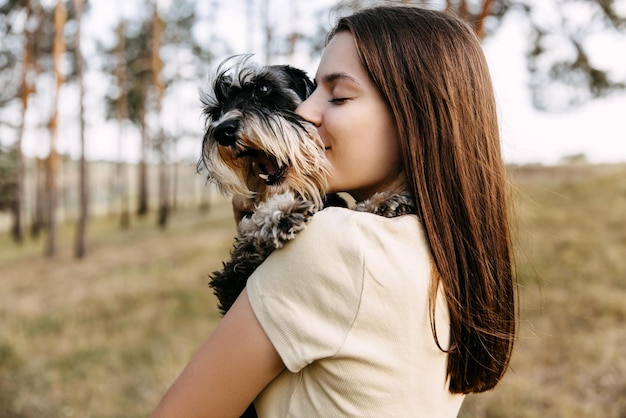 Giovane donna bruna che abbraccia un cane di razza schnauzer in miniatura che lo bacia