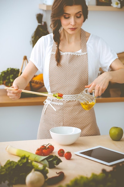 Giovane donna bruna che cucina in cucina. Casalinga che tiene in mano un cucchiaio di legno. Concetto di cibo e salute.