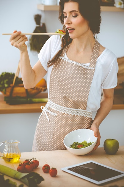 Giovane donna bruna che cucina in cucina. Casalinga che tiene in mano un cucchiaio di legno. Concetto di cibo e salute.