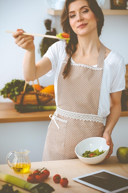 Giovane donna bruna che cucina in cucina. Casalinga che tiene in mano un cucchiaio di legno. Concetto di cibo e salute.