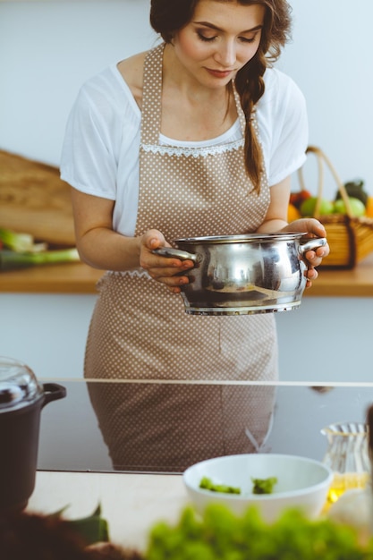 Giovane donna bruna che cucina minestra in cucina. Concetto di cibo e salute.