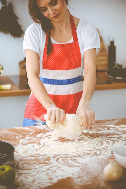 Giovane donna bruna che cucina pizza o pasta fatta a mano in cucina. Casalinga che prepara la pasta sulla tavola di legno. Dieta, cibo e concetto di salute.