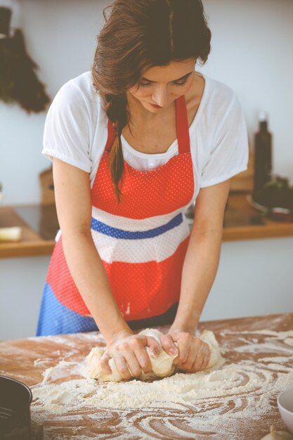 Giovane donna bruna che cucina pizza o pasta fatta a mano in cucina. Casalinga che prepara la pasta sulla tavola di legno. Dieta, cibo e concetto di salute.