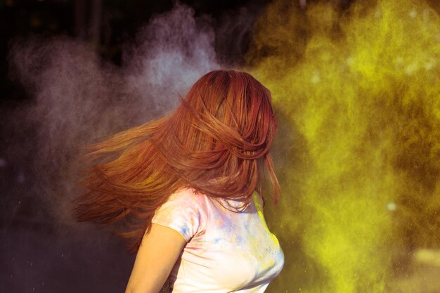 Giovane donna bruna con i capelli lunghi in movimento ricoperta di polvere Gulal colorata