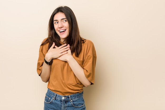 Giovane donna bruna controbeige ridere tenendo le mani sul cuore, della felicità.