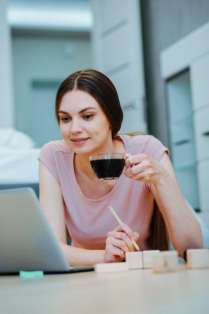 Giovane donna calma che guarda lo schermo del laptop mentre è sdraiata sul pavimento con mattoni di legno al suo fianco