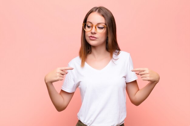 Giovane donna capa rossa che sembra fiero, positivo e casuale che indica il petto con entrambe le mani contro la parete piana