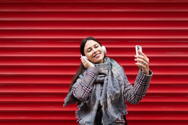 Giovane donna carismatica che balla in cuffia tenendo un telefono cellulare nelle sue mani contro