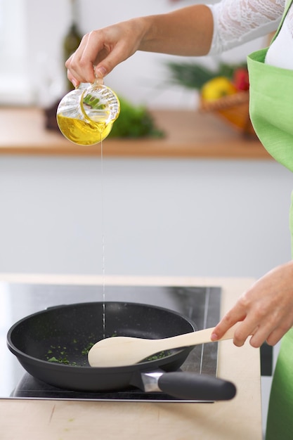 Giovane donna casalinga che cucina in cucina aggiungendo olio d'oliva Concetto di pasto fresco e sano a casa