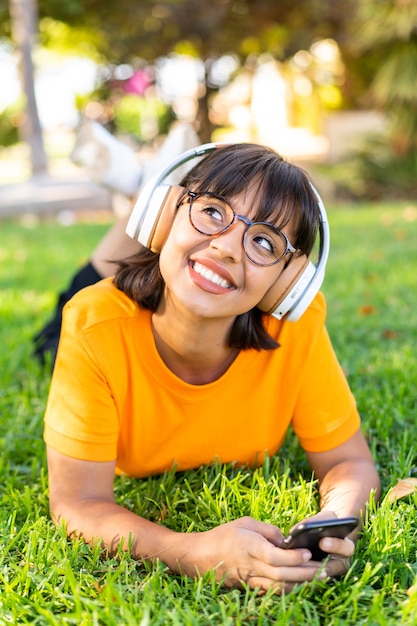 Giovane donna castana all'aperto che ascolta musica con il cellulare e felice