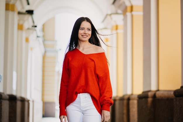 Giovane donna castana attraente soddisfatta che sorride guardando da parte con il bello sorriso Successo