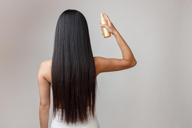 Giovane donna castana che applica lacca per capelli sui capelli