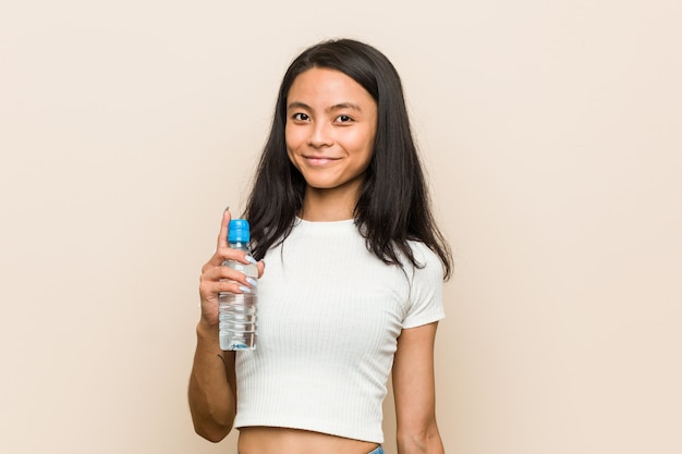 Giovane donna castana che giudica una bottiglia di acqua felice, sorridente e allegra