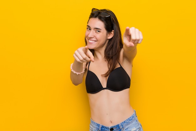 Giovane donna castana che indossa un bikini contro i sorrisi allegri gialli che indicano la parte anteriore.