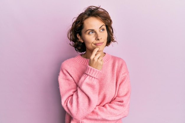 Giovane donna castana che indossa un maglione invernale casual pensando concentrato sul dubbio con il dito sul mento e alzando lo sguardo chiedendosi