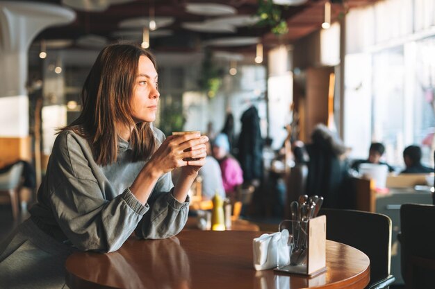 Giovane donna castana che indossa una manica lunga casual godendo il suo caffè seduto nella vita della città del caffè