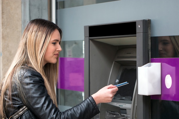 Giovane donna castana che ritira soldi dalla carta di credito