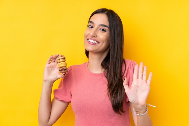 Giovane donna castana che tiene i macarons francesi variopinti e che saluta