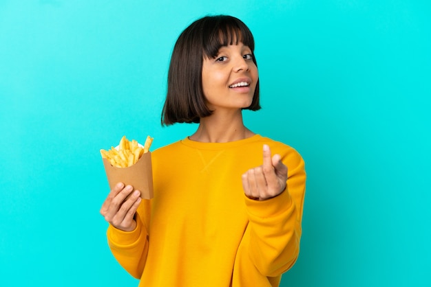 Giovane donna castana che tiene le patatine fritte sopra la parete blu isolata che fa il gesto dei soldi