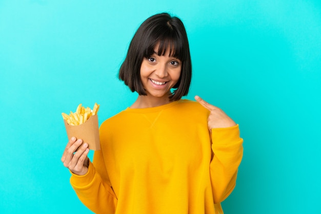 Giovane donna castana che tiene patatine fritte su sfondo blu isolato dando un gesto di pollice in alto