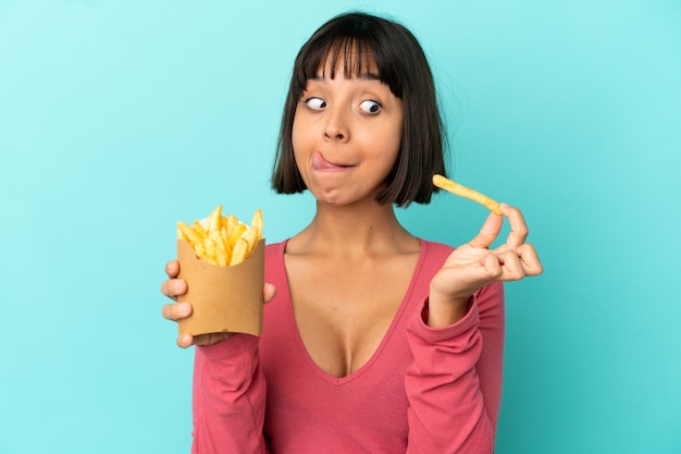 Giovane donna castana che tiene patatine fritte su sfondo blu isolato isolated