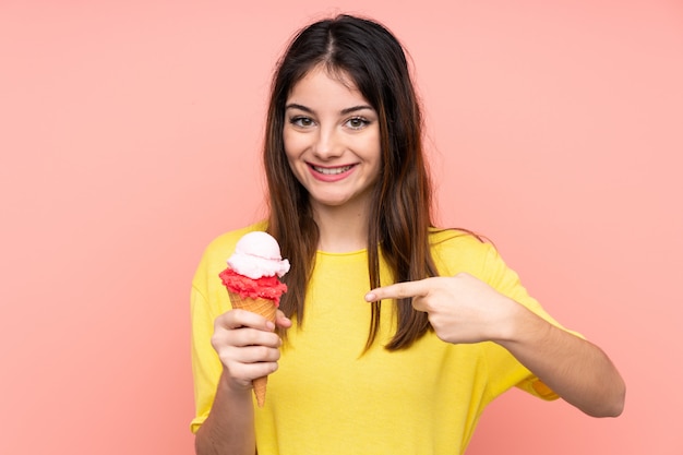 Giovane donna castana che tiene un gelato della cornetta sopra la parete rosa isolata con espressione facciale di sorpresa