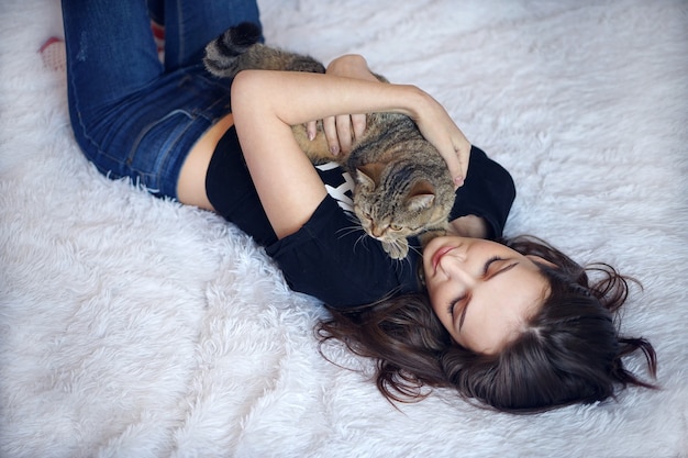 Giovane donna castana con capelli lunghi che gioca con il gatto in camera da letto