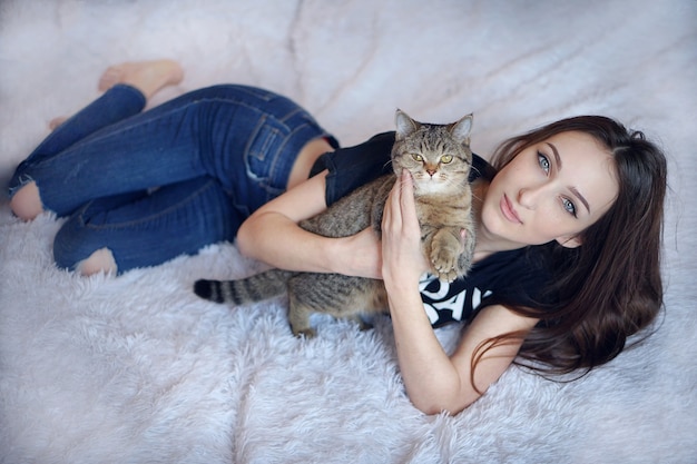 Giovane donna castana con capelli lunghi che gioca con il gatto in camera da letto