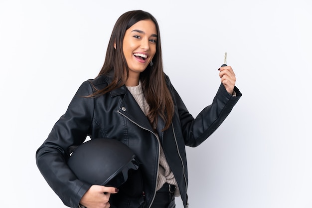Giovane donna castana con un casco del motociclo e tenere una chiave sopra la parete bianca isolata