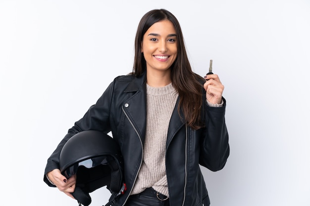 Giovane donna castana con un casco del motociclo e tenere una chiave sopra la parete bianca isolata