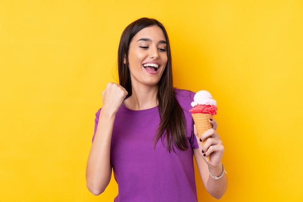 Giovane donna castana con un gelato della cornetta sopra la parete gialla isolata che celebra una vittoria