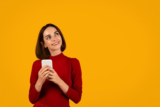 Giovane donna castana curiosa che utilizza smartphone sull'arancia