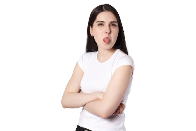 Giovane donna castana dai capelli neri caucasica attraente in maglietta bianca, lingua fuori, prendere in giro l'idea di concetto di donna offesa