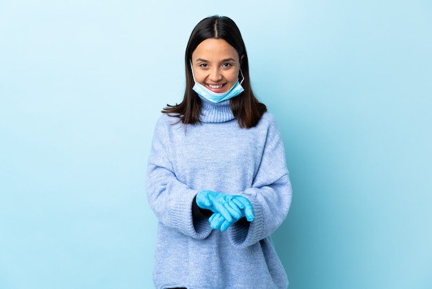 Giovane donna castana della corsa mista che protegge con una maschera e guanti sopra la parete blu che tiene spazio sul palmo