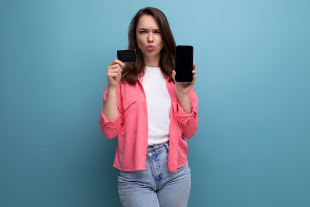 Giovane donna castana di affari di e-commerce in camicia rosa e jeans con il modello della carta dei soldi e del telefono sopra