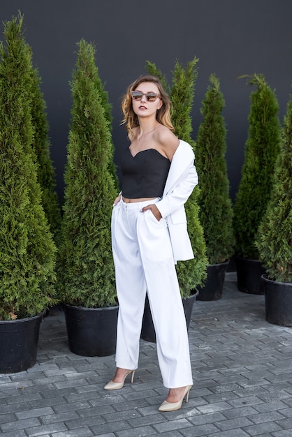 Giovane donna castana felice in vestito bianco che posa alla natura, cedro bianco, ora legale