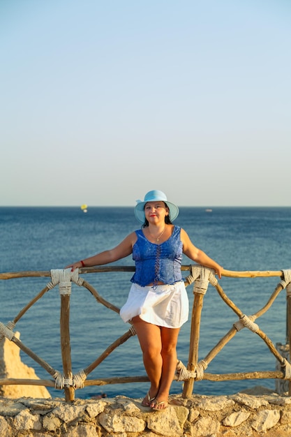 Giovane donna castana in una gonna bianca e un cappello blu in riva al mare felice.