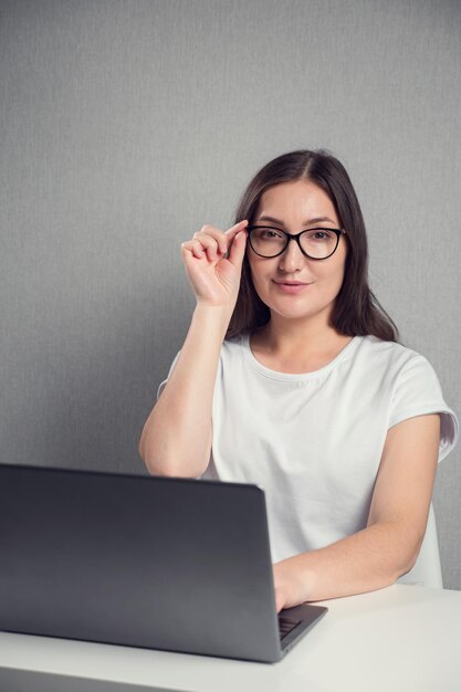 Giovane donna castana in vetri che si siede davanti allo spazio della copia del computer portatile