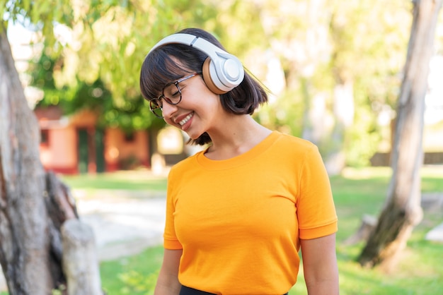 Giovane donna castana nel parco che ascolta musica