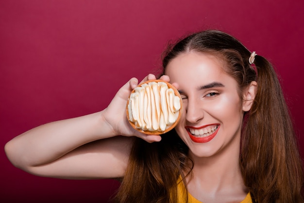 Giovane donna castana piacevole con le labbra rosse che si divertono con la torta crostata al caramello. Spazio vuoto