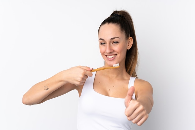 Giovane donna castana sopra la parete bianca isolata con uno spazzolino da denti