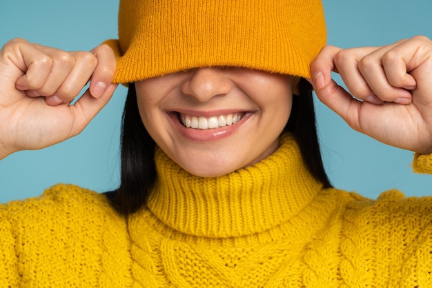 Giovane donna castana sorridente che indossa maglione lavorato a maglia bianco e cappello che posano sul fondo blu dello studio isolato. Concetto di stagione fredda invernale calda