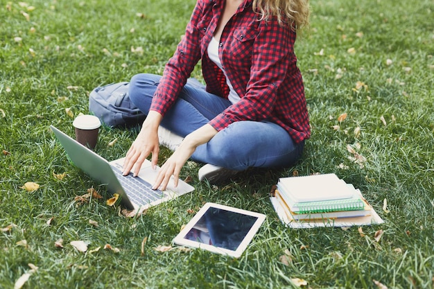 Giovane donna casual con laptop e tablet all'aperto. Studentessa che si prepara per gli esami con computer, libri e caffè nel parco. Istruzione e ingresso nel concetto universitario, ritaglio, spazio di copia.