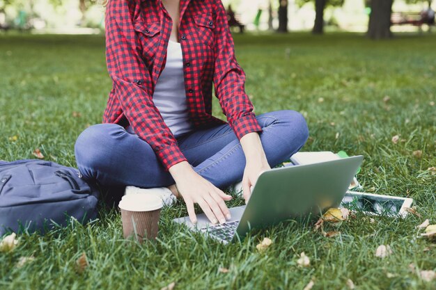 Giovane donna casual con laptop e tablet all'aperto. Studentessa che si prepara per gli esami con computer, libri e caffè nel parco. Istruzione e ingresso nel concetto universitario, ritaglio, spazio di copia.