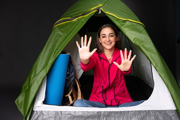 Giovane donna caucasica all'interno di una tenda da campeggio verde contando dieci con le dita